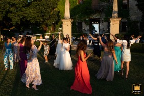 Bancole, Italy - Villa Schiarino reception: As the sun sets, the bride and groom cut ribbons to release the bouquet. Warm light illuminates the outdoor action.